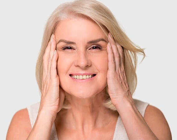 Mujer adulta acaricia su rostro con ambas manos para comprobar resultados de peelings químicos