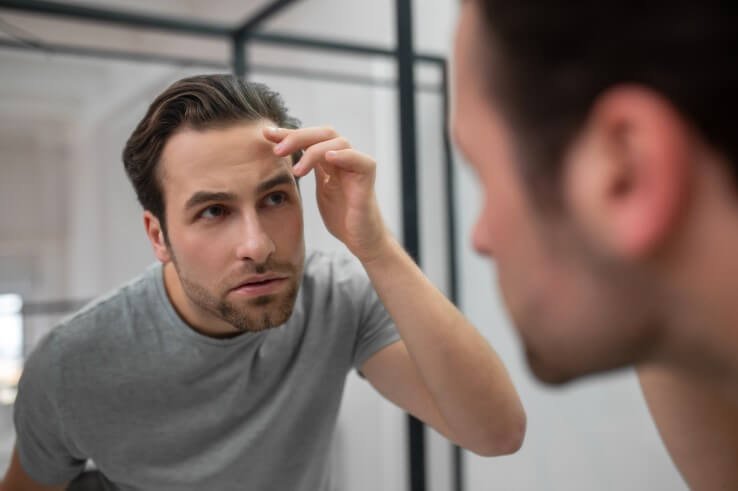 Hombre adulto se toca el rostro en un espejo y decide tomar un tratamiento de rejuvenecimiento 4d de fotona sp dynamis